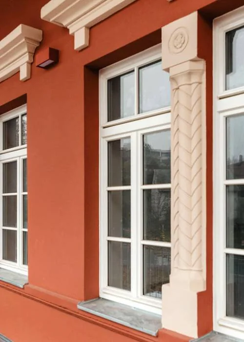Weiße Sprossenfenster in einer roten Fassade mit hellen Verzierungen
